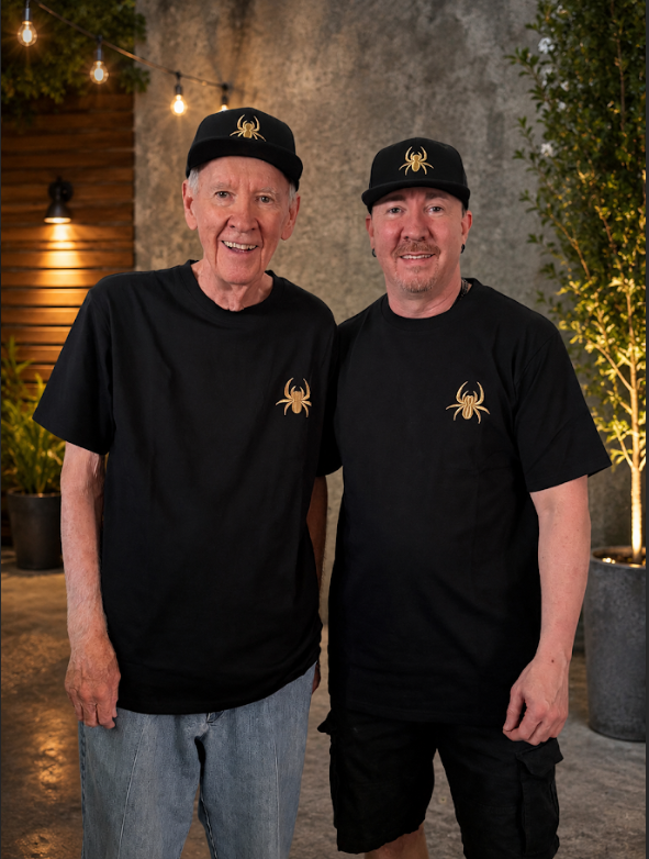 Two people wearing black SilkNook T-shirts and matching hats featuring the gold spider logo, showcasing SilkNook branded apparel.