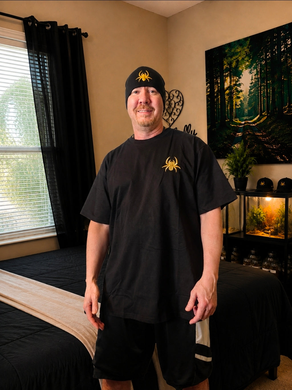 Man wearing a black SilkNook beanie and matching black T-shirt, both featuring gold embroidered jumping spider logos.