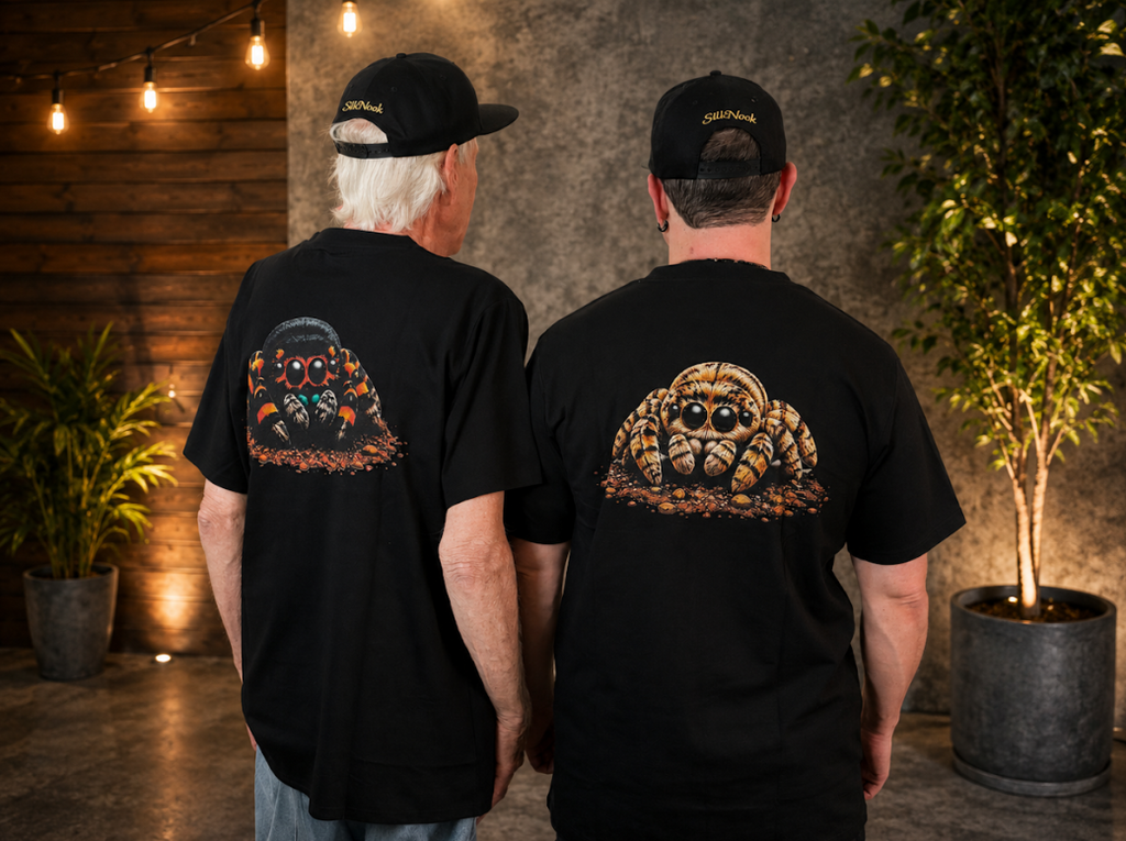 Black SilkNook T-shirt featuring a detailed orange and black jumping spider design on the back, displayed against a warm natural-inspired background.